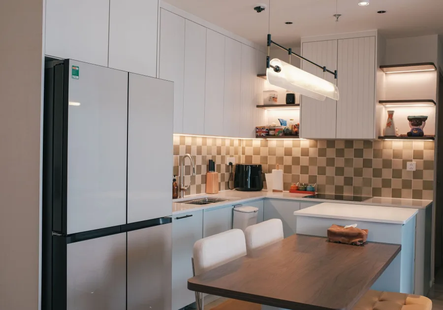 Tall stainless steel refrigerator standing in a bright fitted kitchen